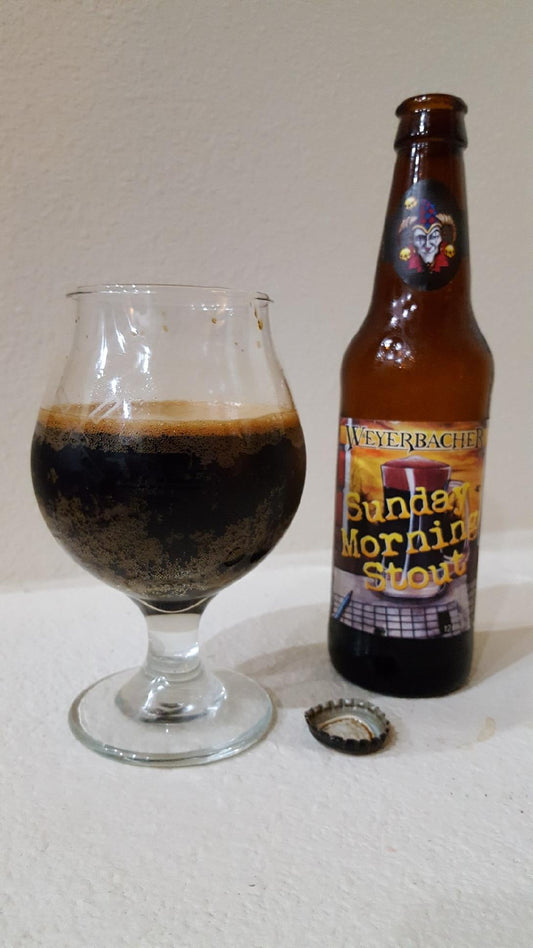 Weyerbacher Sunday Morning Stout poured into a tulip glass beside the bottle, pitch black with a thin collapsed tan head